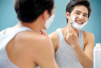 快乐的青年男人对着镜子刮胡子刮胡刀高质量图片