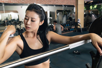 健身房里年轻女子扶着杠铃展示肌肉