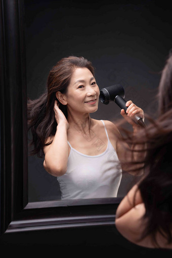 <strong>中年女人</strong>对着镜子用吹风机吹头发站着高端拍摄