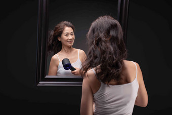 中年女人对着镜子用吹风机吹头发仅女人清晰图片