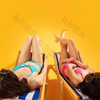 比基尼闺蜜坐在沙滩上日光浴黄色背景高端摄影