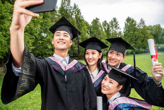 四个身穿学士服的大学生用手机自拍