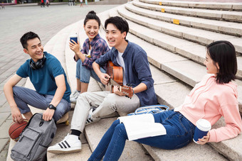 年轻的大学生坐在台阶上弹吉他坐着高清镜头