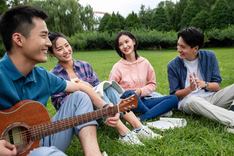 快乐的大学生在草地上弹吉他唱歌拍手场景
