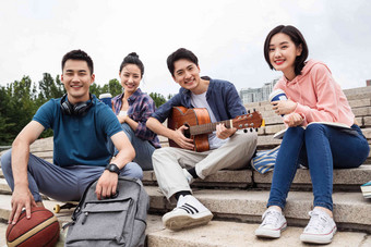 年轻的大学生坐在台阶上弹吉他四个人清晰素材