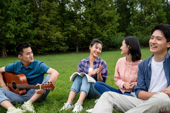 快乐的大学生在草地上弹吉他唱歌东方人清晰摄影图
