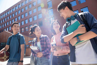 阳光下四个大学生在校园里边走边聊讨论氛围摄影图