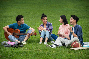 快乐的大学生在草地上弹吉他唱歌相伴写实相片