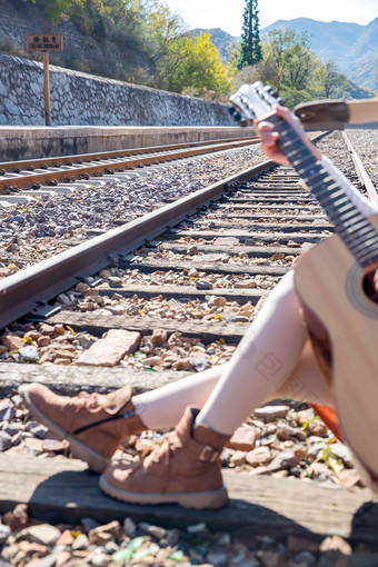 青年女人坐在铁路边弹吉他