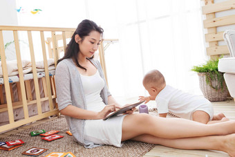 年轻妈妈在家边看孩子边使用电脑