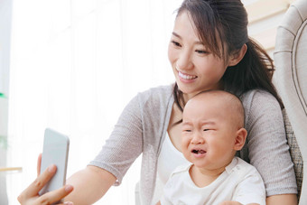年轻妈妈和宝宝用手机照相面部表情氛围摄影