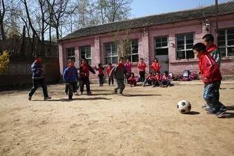 乡村小学生在学校里踢足球球场写实摄影