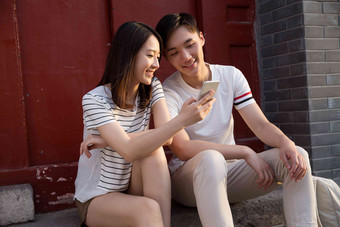 青年情侣坐在门口看手机东亚高质量摄影图