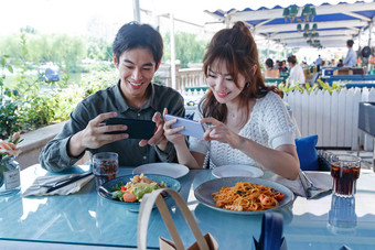 青年情侣在餐厅里用手机拍照两个人高端摄影图