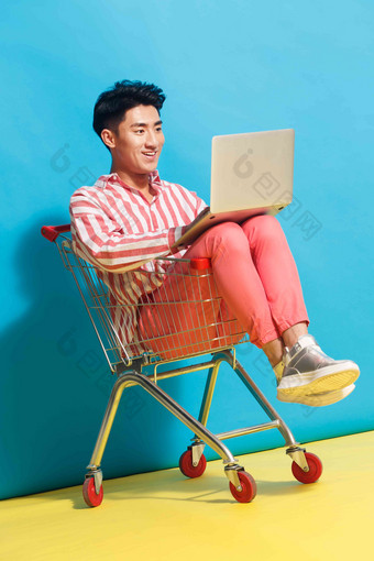 青年男人坐在购物车里用笔记本电脑一个人高端素材