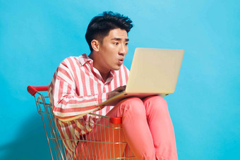 青年男人坐在购物车里用笔记本电脑促销氛围拍摄