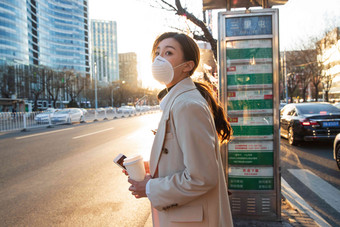 戴口罩的年轻女人站在公交车站