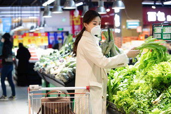 戴口罩的青年女人在<strong>超市</strong>挑选青菜