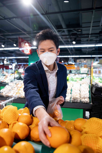 戴口罩的青年男人在超市挑选水果