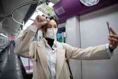 戴口罩的年轻女人在地铁里看手机