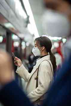 戴口罩的年轻女人在地铁里看手机