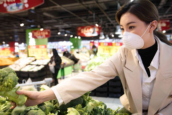 戴口罩的青年女人在超市购买蔬菜