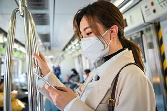 青年女人在地铁上看手机防流感口罩摄影图