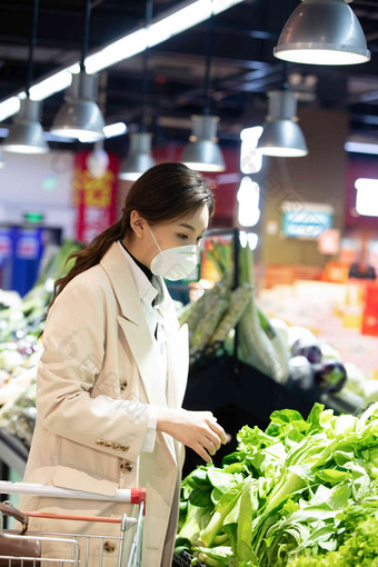 戴口罩的青年女人在超市购买青菜