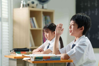 在课堂上举手的小学生课桌高端拍摄