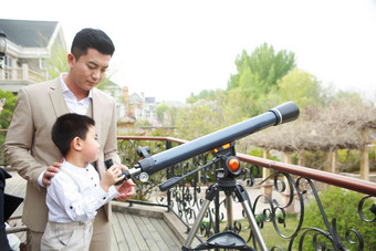 父亲和儿子在阳台使用天文望远镜城市生活影相