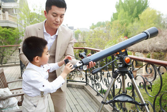 父亲和儿子在阳台使用天文望远镜父亲素材