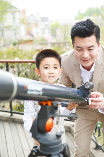 父亲和儿子在阳台使用天文望远镜两个人照片