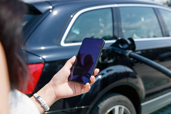 青年女人使用手机自助充电汽车