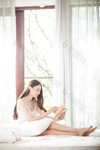 青年女人坐在<strong>床上</strong>看书