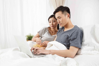 青年情侣坐着床上看电脑床氛围照片