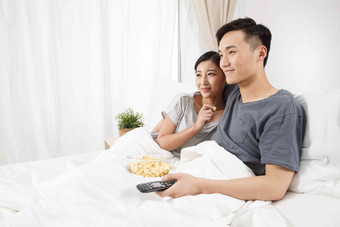 青年情侣坐着床上看电视紧张氛围影相