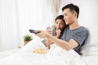 青年情侣坐着床上看<strong>电视</strong>中国人高端图片