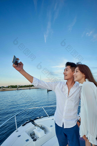 青年夫妇站在游艇上用手机拍照东亚素材