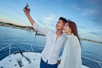 青年夫妇站在游艇上用手机拍照天空高清素材