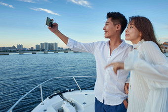 青年夫妇站在游艇上用手机拍照甲板氛围摄影
