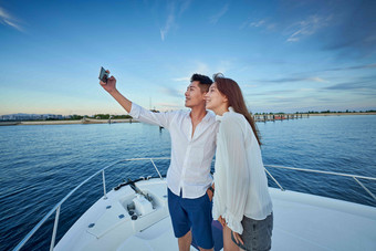 青年夫妇站在游艇上用手机拍照休闲图片