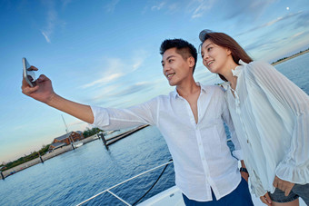 青年夫妇站在游艇上用手机拍照情侣高端场景