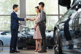 汽车销售人员和青年夫妇握手站着写实场景