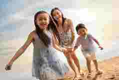 年轻母亲牵着两个孩子在沙滩上奔跑