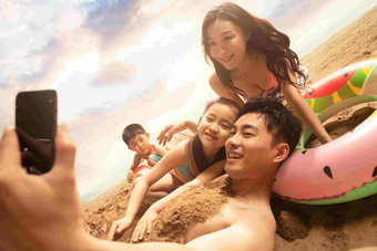 沙滩上男人拿<strong>手机</strong>和妻子孩子自拍