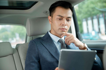 商务男士坐在汽车里看平板电脑
