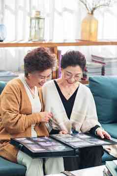 快乐的中老年姐妹坐在沙发上看相册爱氛围相片