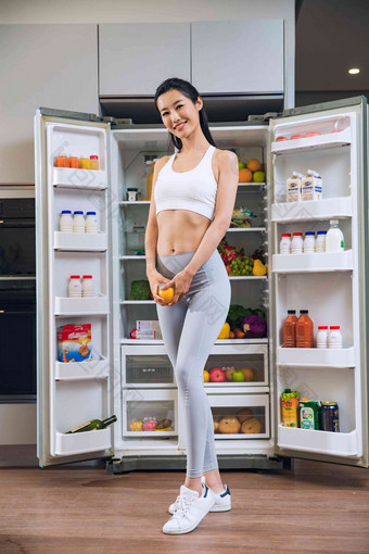 穿着运动装的青年女人站在冰箱前膳食清晰场景