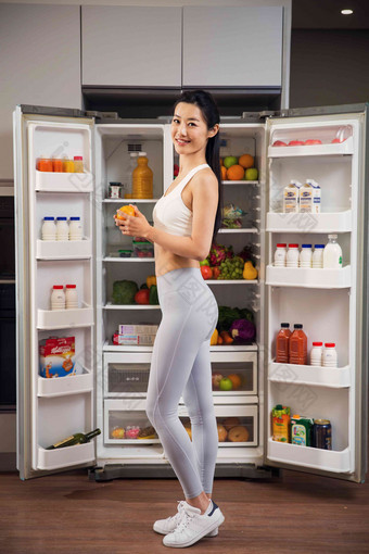 穿着运动装的青年女人站在冰箱前彩色图片写实相片