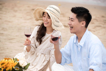 浪漫的青年夫妇坐在沙滩上喝红酒